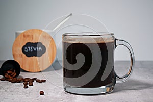 A glass of black coffee and a bowl with stevia sweetener, grey background