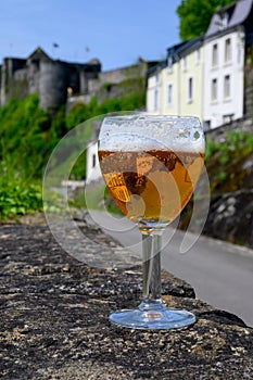 Glass of blond strong Belgian abbey beer on old castle wall in sunny day with nice view on old town Bouillon, Belgium