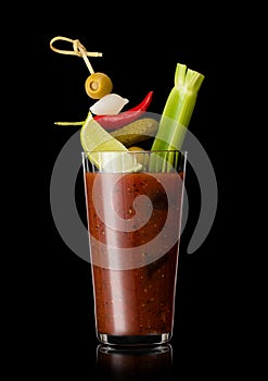 Glass of bloody mary cocktail mix with black pepper and celery on black background with pickle and olive