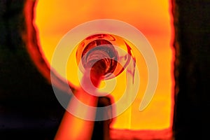 Glass blower working on a bubble of melted glass on a rod by heating it up in a kiln at a glass maker& x27;s workshop