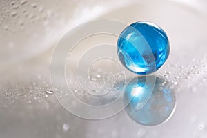 Glass blue ball on a white glass table. Abstract photo with glass and reflection.