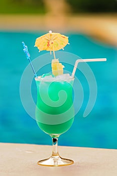 Glass of blue cocktail at swimming pool in summer time