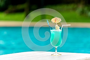 Glass of blue cocktail at swimming pool in summer time