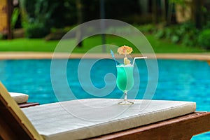 Glass of blue cocktail at swimming pool in summer time