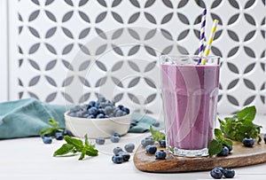 Glass of blueberry smoothie with mint and fresh berries on white wooden table, space for text