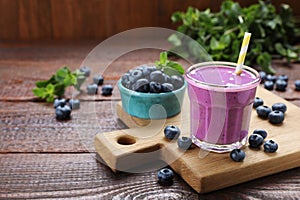 Glass of blueberry smoothie with mint and fresh berries on wooden table. Space for text