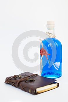 Glass bottle with blue Curacao alcohol color on white background. brown leather notebook