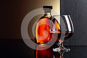 Glass and bottle of brandy on a black reflective background