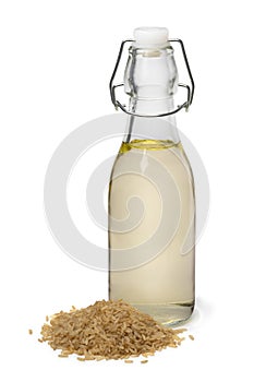 Glass bottle with brown rice vinegar and a heap of brown rice in front on white background close up