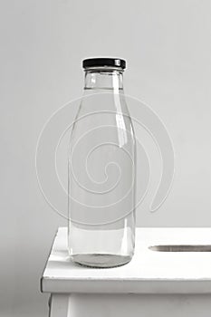 Glass bottle with clear water on a wooden chair on a white wall background