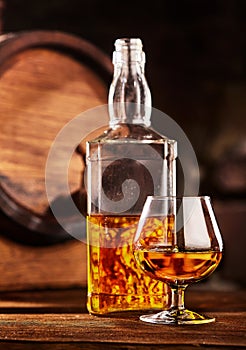 Glass and bottle of Cognac on wodden table old oak barrel defocussed