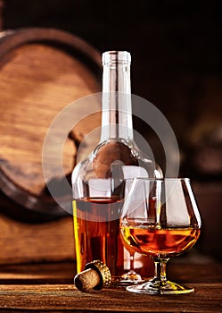 Glass and bottle of Cognac on wodden table old oak barrel defocussed