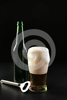 Glass and bottle of cold beer with opener on dark background