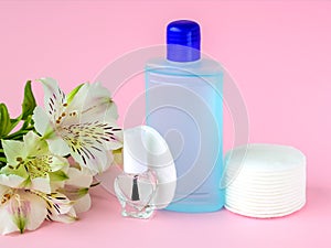 Glass bottle with colorless nail polish, plastic bottle with nail varnish remover, cotton pads and white flowers on a pastel pink