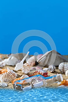 A glass bottle with a letter washed up on the beach shore. Sea beach full of shells and sand. Blue sky. Clean water