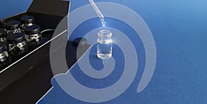 Glass bottle of cosmetics dosing with pipette with sparkling drop,vials in box behind,on blue background.Copy space