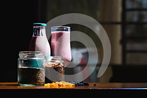Glass bottle with a cup of juice, two spice jars and dry fruits on a wooden table against blur