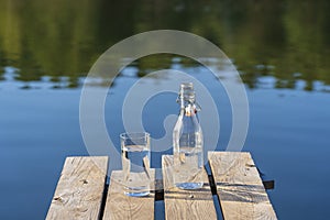 Glass and bottle with drinking water on a wooden pier in the morning near the lake. Nature and travel concept