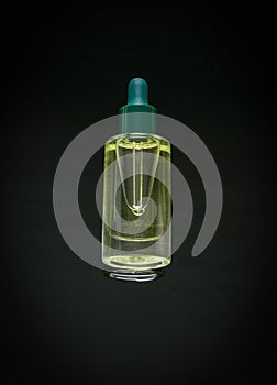 A glass bottle with an eyedropper filled with aromatic oil on a black background