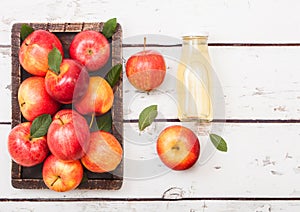 Glass bottle of fresh organic apple juice with pink lady red apples in vintage box on wooden background
