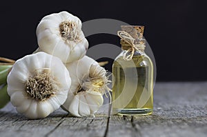 Glass bottle of garlic oil and Ripe and fresh garlic plant on wooden or rustic table