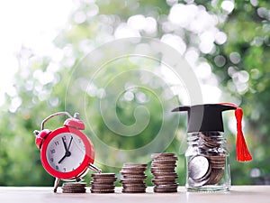 Glass bottle with graduation hat and red alarm on stack of coins. The concept of saving money for education, student loan,