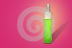 Glass bottle with green refreshing herbal drink in pink background