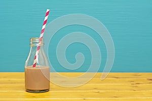 Glass bottle half full with chocolate milkshake with paper straw