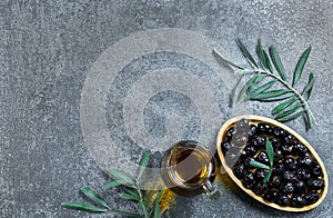 Glass bottle of homemade olive oil and olive tree branch, raw turkish black olive seeds and leaves on grey rustic table