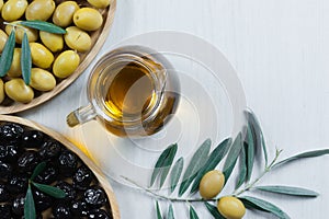 Glass bottle of homemade olive oil and olive tree branch, raw turkish green and black olive seeds and leaves on white table