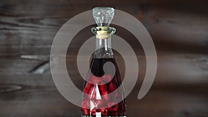 Glass bottle homemade red raspberry liqueur on a wooden background, rotates