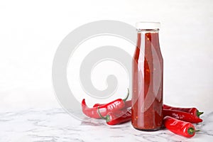 Glass bottle of hot chili sauce with peppers on table