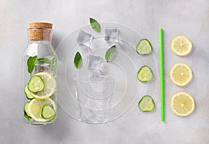 Glass bottle with infused water with lemon, cucumber, mint, ice and an empty glass