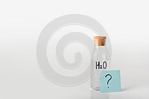 Glass bottle with the inscription chemical formula of water on it and question mark on a note sheet.