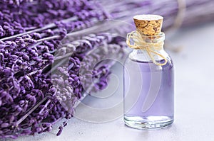 Glass bottle of Lavender essential oil with dried lavender flowers and seeds on white table