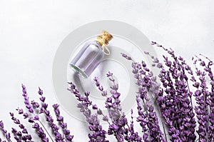 Glass bottle of Lavender essential oil with dried lavender flowers and seeds on white table