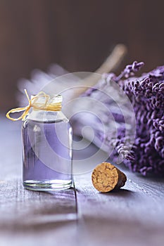 Glass bottle of Lavender essential oil with dried lavender flowers and seeds on white table