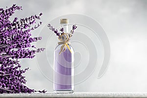 Glass bottle of Lavender essential oil with dried lavender flowers and seeds on white table