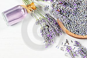 Glass bottle of Lavender essential oil with fresh lavender flowers and dried lavender seeds on white rustic table