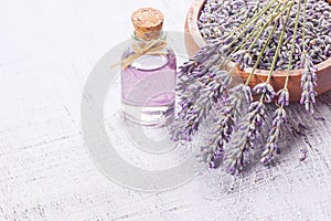 Glass bottle of Lavender essential oil with fresh lavender flowers and dried lavender seeds on white rustic table