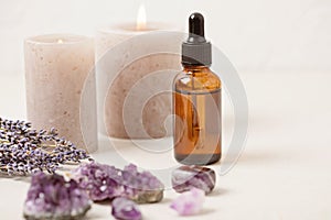 Glass bottle of Lavender essential oil with lavender flowers and candles and amethyst crystals