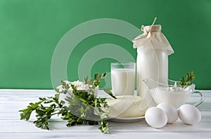 Glass and a bottle of milk, a plate of cottage cheese, cheese, white raw eggs, sour cream in a gravy boat, sprigs of parsley on a