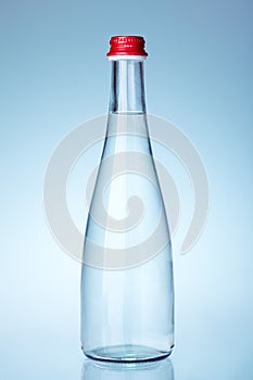 Glass bottle of mineral water with red cap filled with liquid.