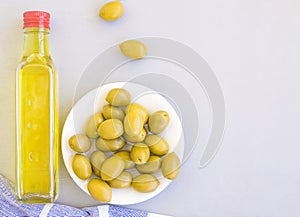 A glass bottle of olive oil, a bowl of olives, and a towel. Grey background, space for text.