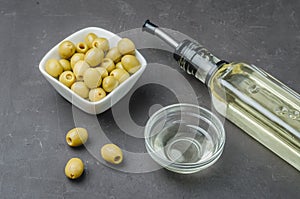 Glass bottle of olive oil and olive in a white bowl on a dark background. Top view. Olive oil concept