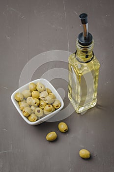 Glass bottle of olive oil and olive in a white bowl on a dark background. Top view. Organic olive oil concept