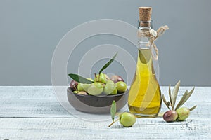 Glass bottle of olive oil and wooden breakfast bowl with raw turkish olive seeds and leaf on white rustic vintage table. Olives b