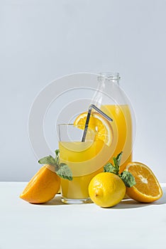 Glass and bottle of orange juice with mint, half fresh orange, lemon, grey background