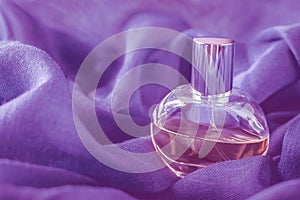 Glass bottle with perfume on background of very peri purple fabric. Macro close-up photo with copy space, soft focus