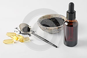 Glass bottle and pills of black cumin seeds essential oil. Nigella Sativa in spoon and bowl on white background